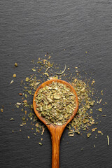 Wooden spoon with mixed dried fine herbs on a dark slate background