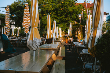 Folded and closed large outdoor umbrellas, tables and chairs in street eatery or cafe in Europe.