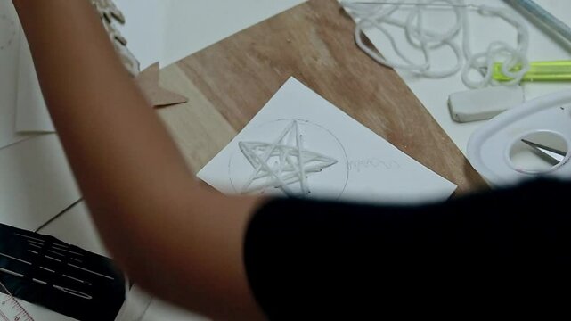 Diluting and mixing yellow color before painting a circle around a star shape sewn with white yarn to make a parol of Philippine Christmas lantern card design