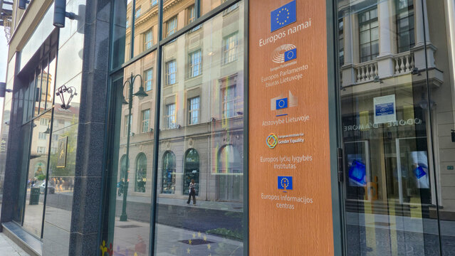 Vilnius Lithuania - 06.14.2025 European Union institutions listed on a wood-paneled sign outside a modern glass building with reflections of historical architecture in the background