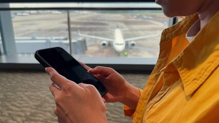 A seated traveler texts on a smartphone with planes visible outside the airport terminal large windows. Captures the essence of modern travel and connectivity. Closeup of hands navigating on a phone - Powered by Adobe