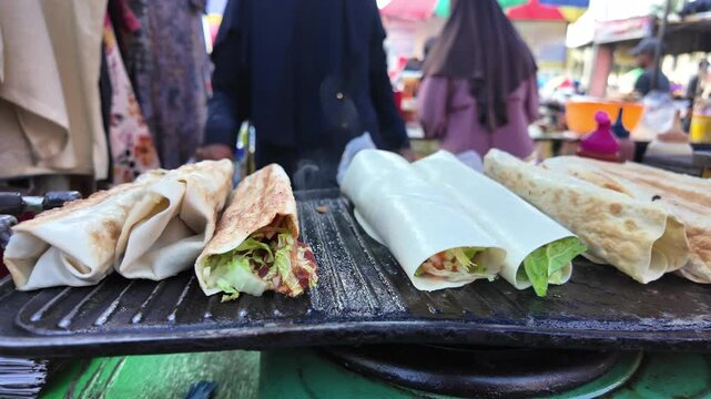 Street Food Jember Town Square, Indonesia - 17 June 2025: Hands of a Seller Brushing Kebab Wraps with Melted Butter on a Flat Griddle.