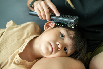 Asian boy lies on his mother's lap, using a comb to comb her hair.
