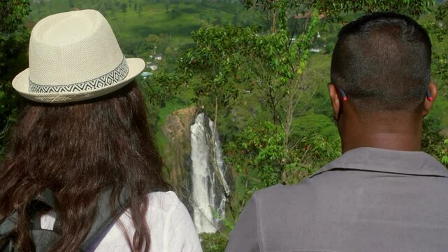 Travelers standing near cascading Ramboda Falls, surrounded by verdant tropical rainforest vegetation, capturing scenic beauty of Sri Lankan landscape while experiencing natural wilderness