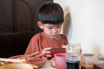 Asian boy playing with mobile phone while eating