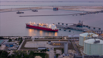 Aerial view of an LNG tanker docked at an offshore terminal with multiple pipelines, storage tanks,...
