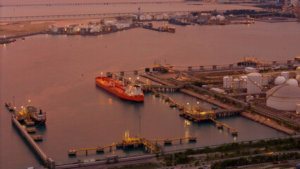 large oil tanker docked at a refinery terminal with multiple white storage tanks, complex pipeline...