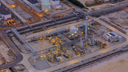 large industrial oil and gas storage tanks at a coastal refinery terminal during dusk. Tanker ships...