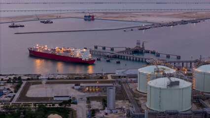 LNG tanker docked at an offshore terminal with multiple pipelines, storage tanks, and an industrial...