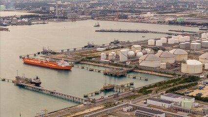 large oil tanker docked at a refinery terminal with multiple white storage tanks, complex pipeline...
