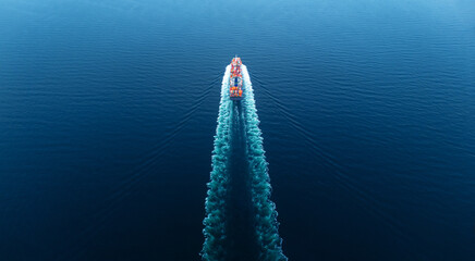 Stern of Cargo Container Ship sailing through deep blue ocean waters, leaving a vibrant symmetrical...