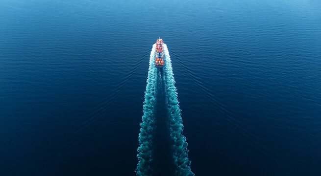 Stern of Cargo Container Ship sailing through deep blue ocean waters, leaving a vibrant symmetrical wake behind. Express Container ship running very fast.