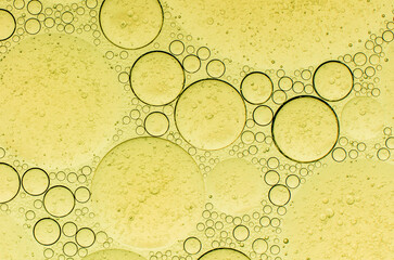 Macro abstract image of golden oil bubbles suspended in liquid, forming overlapping circular...