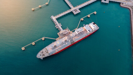 Aerial view of an LNG tanker docked at an offshore terminal with multiple pipelines, storage tanks, and an industrial complex. Captures global energy logistics