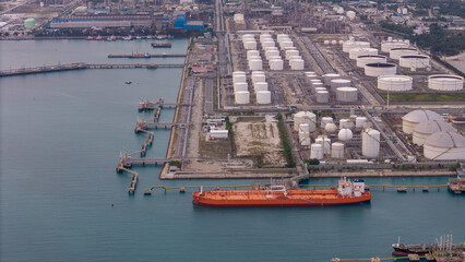 large oil tanker docked at a refinery terminal with multiple white storage tanks, complex pipeline networks, and offshore loading platforms. Represents global oil logistics