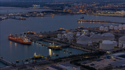 large oil tanker docked at a refinery terminal with multiple white storage tanks, complex pipeline networks, and offshore loading platforms. Represents global oil logistics