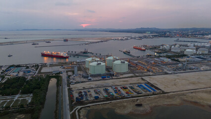 Aerial view of an LNG tanker docked at an offshore terminal with multiple pipelines, storage tanks, and an industrial complex. Captures global energy logistics
