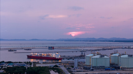 Aerial view of an LNG tanker docked at an offshore terminal with multiple pipelines, storage tanks, and an industrial complex. Captures global energy logistics