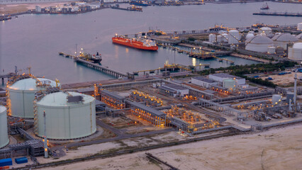 large oil tanker docked at a refinery terminal with multiple white storage tanks, complex pipeline networks, and offshore loading platforms. Represents global oil logistics