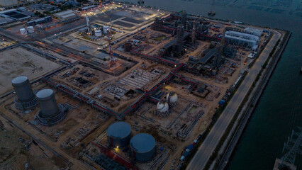 large industrial oil and gas storage tanks at a coastal refinery terminal during dusk. Tanker ships docked at long piers highlight the global energy transport infrastructure.