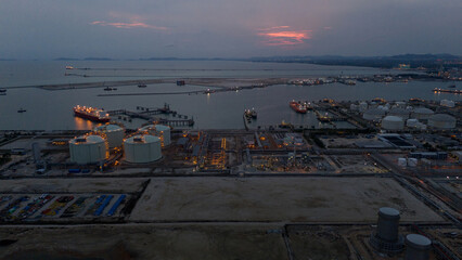 Aerial view of an LNG tanker docked at an offshore terminal with multiple pipelines, storage tanks, and an industrial complex. Captures global energy logistics