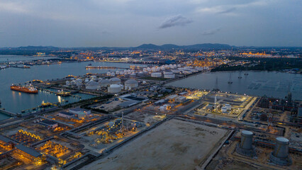 large industrial oil and gas storage tanks at a coastal refinery terminal during dusk. Tanker ships docked at long piers highlight the global energy transport infrastructure.