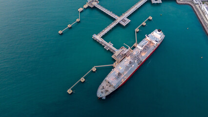 Aerial view of an LNG tanker docked at an offshore terminal with multiple pipelines, storage tanks, and an industrial complex. Captures global energy logistics
