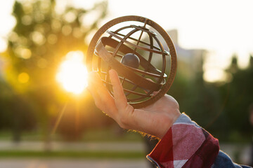 Hand holding antique metal globe against sunset in park. Armillary sphere on hand, spherical...