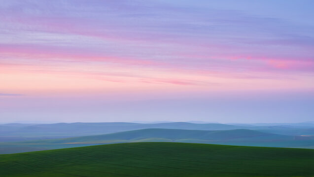Serene pastel sky with fluffy clouds gently floating above smooth rolling hills, creating a calm and dreamy landscape.