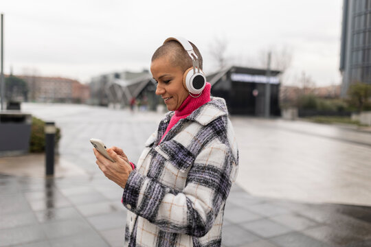 Smiling business woman wearing headphones using smartphone in the city