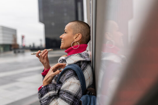 Smiling business woman sending a voice message on her smartphone in the city - Powered by Adobe