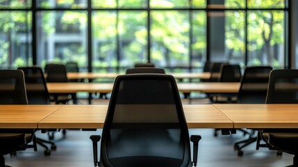 Modern office interior featuring empty desks and chairs with large windows showing greenery