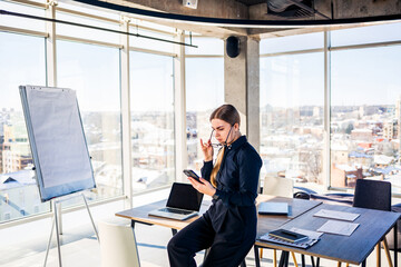 In a modern office with views of the city skyline, a dedicated businesswoman focuses on her tasks,...