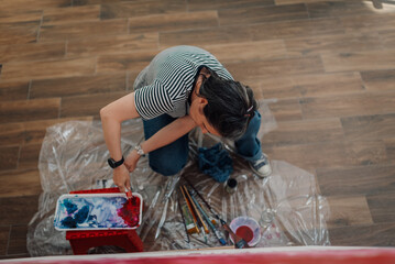 Woman artist preparing paint for wall mural, mixing colors on palette