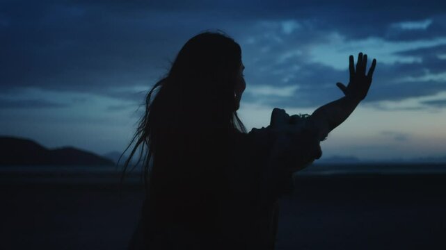 Woman finding inner peace in nature. Silhouette of young woman standing in beautiful natural landscape with mountains, opening her arms and enjoying dramatic dusk light and wind moving her hair