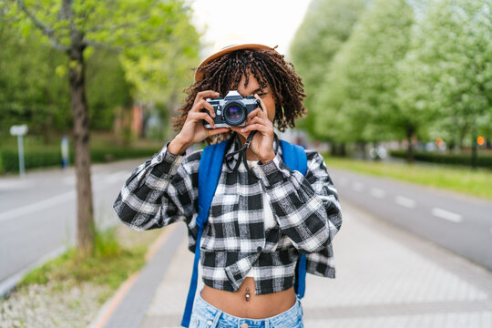 Young woman with backpack and vintage camera taking photos in an urban park, enjoying her passion for photography