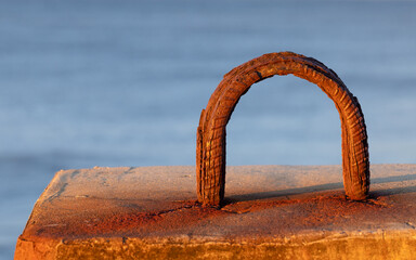  A weathered and textured mooring ring embedded in concrete, and rusted by the harsh coastal environment, catches the warm light of the setting sun in Ballina, New South Wales, Australia.