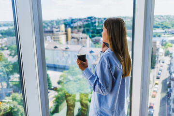 A contemplative woman is savoring a cup of coffee while taking in a breathtaking scenic view of the city skyline from her chic modern apartment. This moment encapsulates balance and mindfulness