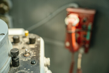 A dusty control panel with multiple knobs and dials is shown in focus on a naval vessel. A red...