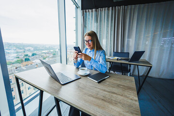 A dedicated businesswoman works remotely in her stylish office with a city view, using her smartphone to stay connected and productive, highlighting her commitment to innovative telecommuting