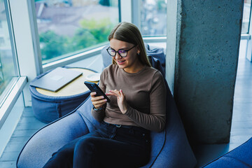 A young woman is happily engaging with her smartphone in a cozy and stylish workspace, embodying a sense of comfort and connectivity that reflects the latest modern lifestyle trends we see around us
