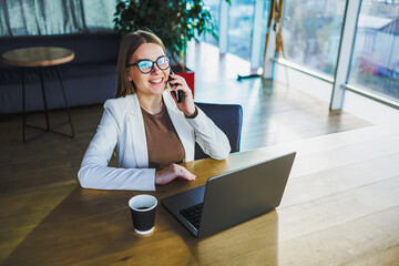 In a modern office, a professional woman is on a crucial business call, her laptop open and a fresh cup of coffee by her side, showcasing her focus and productivity during work hours