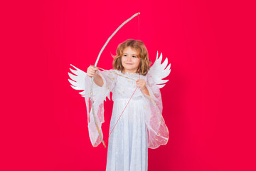 Angel kid shoots a love arrow from a bow on Valentines Day. Angel child. Isolated studio shot. Cute kid with angel wings. Cupid, valentines day concept.
