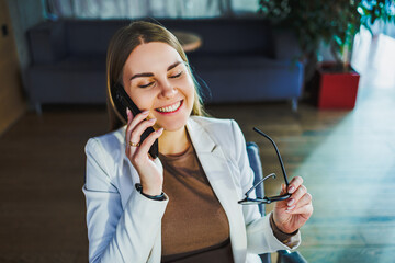 A confident businesswoman engages in a focused phone call, seated comfortably in a modern office, exuding professionalism as she effectively manages business matters and communication