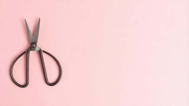 Open metal scissors with black handles placed on a solid light pink background with a large area of negative space ready for text or design.