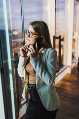 A professional businesswoman is deeply engaged in an important phone call in a modern office, characterized by stunning views of the city skyline that inspire productivity and innovation