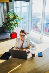 A dedicated professional woman is focused on working diligently on her laptop while seated in a modern office environment, showcasing her commitment to her tasks and responsibilities