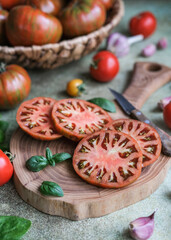 Sliced tomatoes with fresh basil leaves on wooden cutting board, ready for healthy meal