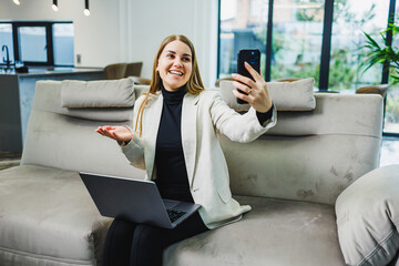 A professional businesswoman is actively engaged in a video call while comfortably seated on her couch, using her laptop to facilitate effective communication and collaboration with team members