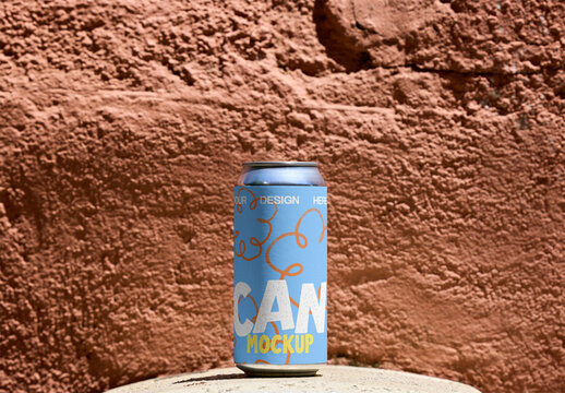Blank beverage can stands upright against a rough, earthy colored wall, showcasing its adaptable design for branding or marketing. PSD template mockup.